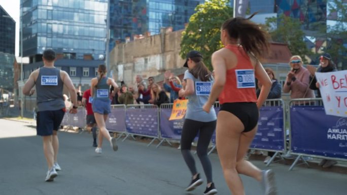 后景:不同群体的马拉松慢跑者争夺第一名，在城市小道上跑步。观众为参加比赛的亲人鼓掌欢呼