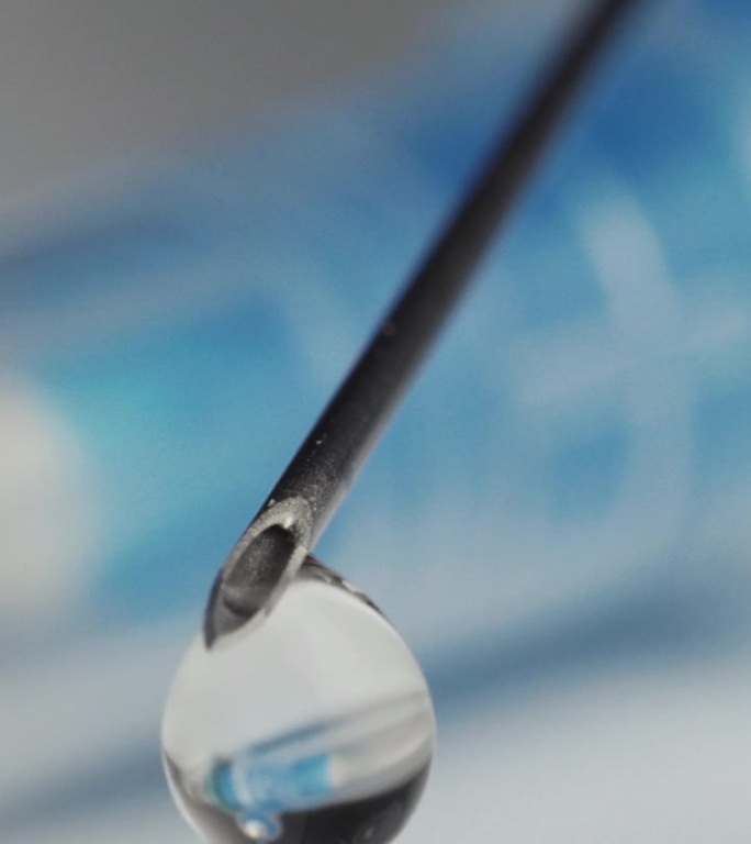 注射器从针头上滴入疫苗的医疗注射器一滴的倒影。特写镜头。垂直视频。