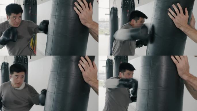 亚洲男拳击手在体育中心教练的指导下用沙袋训练