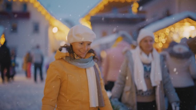 两个女人扛着一棵圣诞树穿过下雪的圣诞市场。圣诞集市上的欢乐时光。