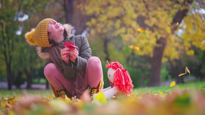 秋天的公园和快乐的女孩在户外玩着黄色的落叶