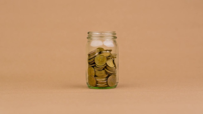 玻璃瓶里的硬币数量在减少。投资。股息。的薪水。现金流。每天的钱。金钱和时间的概念。
