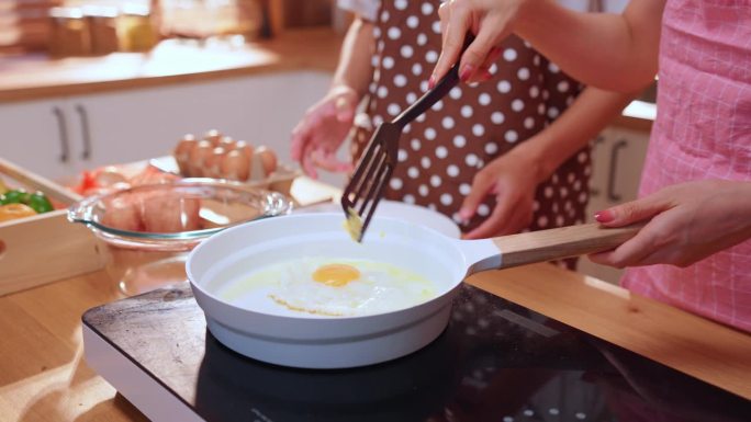近距离拍摄一对年轻夫妇在家里厨房的平底锅上煎鸡蛋的手。有魅力的男女心情愉悦，心情放松，享受烹饪早餐的