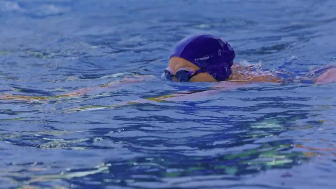 一名职业女游泳运动员在泳池边戴着护目镜的侧视图。一位女游泳者跳入水池。特写，慢镜头。