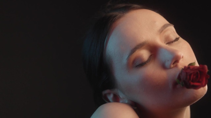 性感的女人用红色的口红和纹身工作室拍摄诱人的拿着一个红色的玫瑰在嘴里