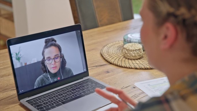 一个女人在笔记本电脑屏幕上和一个在家工作的女人进行视频会议