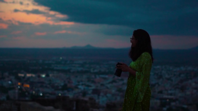 古吉拉特邦古吉拉特邦库奇市，年轻的印度女子手持相机观看布吉市的剪影。女摄影师在深夜拍摄。旅游和假期的