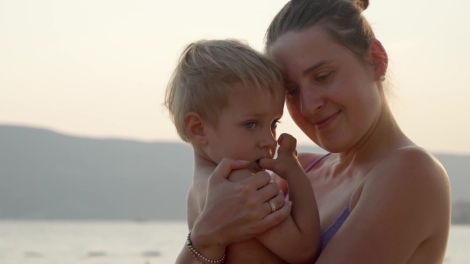 夕阳下的海滩上，母亲抱着儿子的剪影。假期、暑假、旅游。