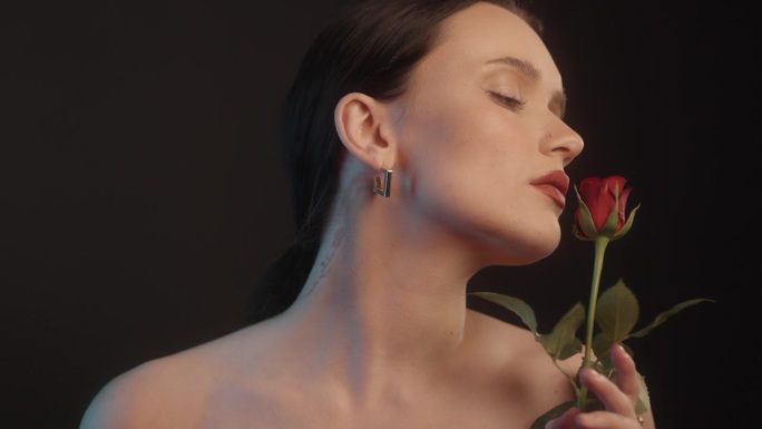 美丽感性的女人与红色的口红黑色背景工作室拍摄的姿势，看着单一的红玫瑰