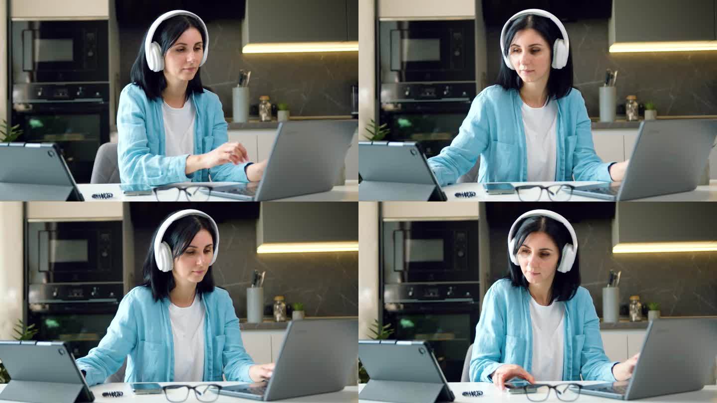 商务女性无线耳机坐在办公桌上使用笔记本电脑在家里有创意的年轻女性浏览互联网和管理社交媒体。e - l