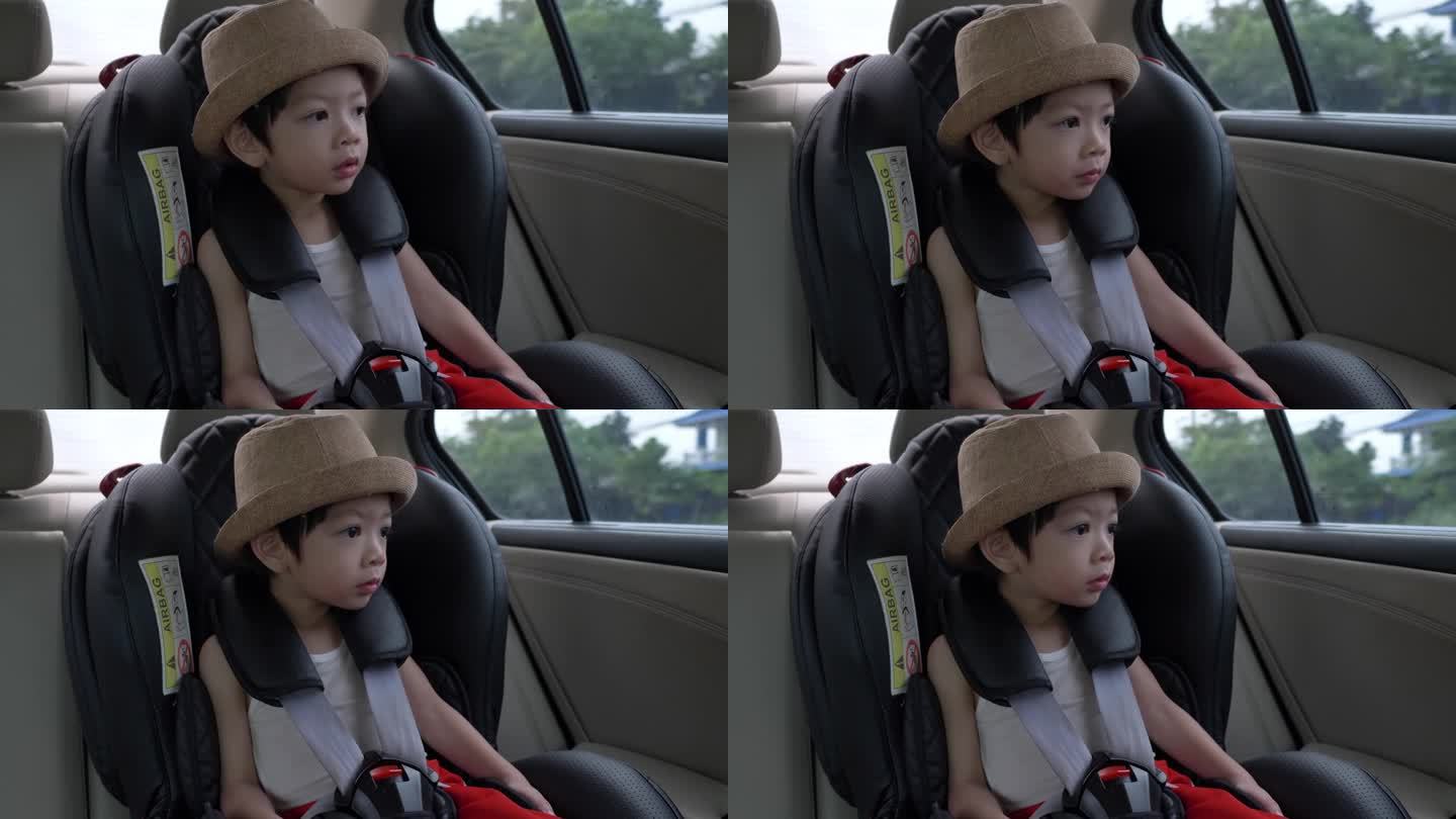 可爱的小男孩戴着帽子坐在安全座椅上，看着窗外的阳光明媚，慢动作的场景