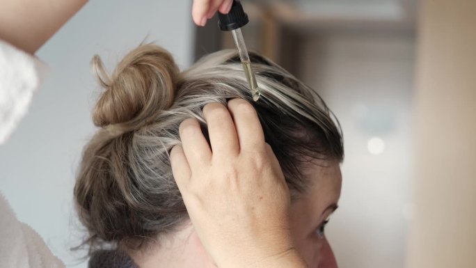 女人用移液管往头发上抹油。美容护理头皮和头发。