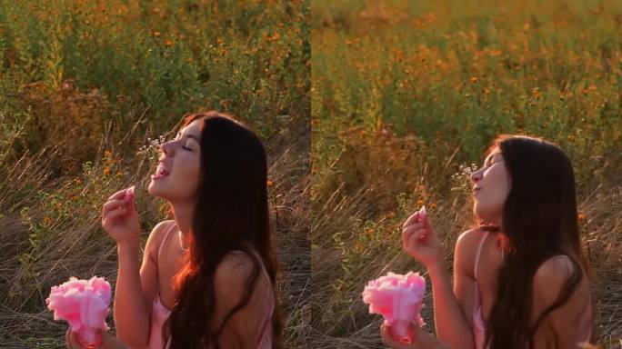 夕阳下，年轻女子在田野里吃粉红色的棉花糖。快乐时光，消磨时光。假期