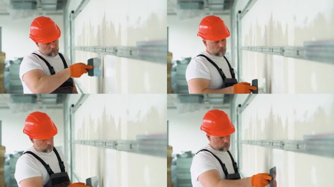 一名穿制服的工人在石膏板上涂灰泥。干墙板接缝处腻子
