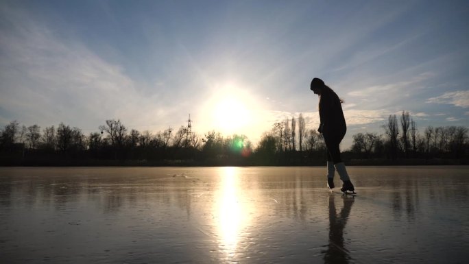 年轻女子正在滑冰。女孩在冰冻的湖泊或河流上独自训练。女士在户外提高他的技能。耀眼的阳光反射在冰面上。