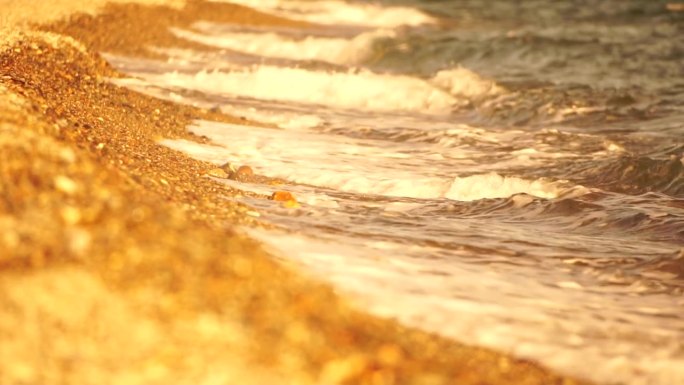 小海浪，模糊的软泡沫海浪冲刷金色卵石沙滩夕阳。海滩上的海浪。没有人。假日休闲概念。抽象航海夏季海洋日