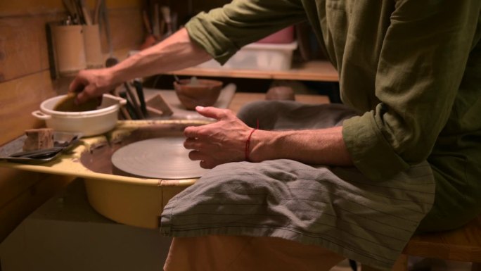 陶工师傅用湿海绵清洗旋转的陶轮。手力强的人，家手艺好