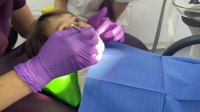 一位戴着医用口罩和紫色橡胶手套的牙医给一个蹒跚学步的小男孩戴上了印章。牙科治疗、检查、小儿牙科。高品