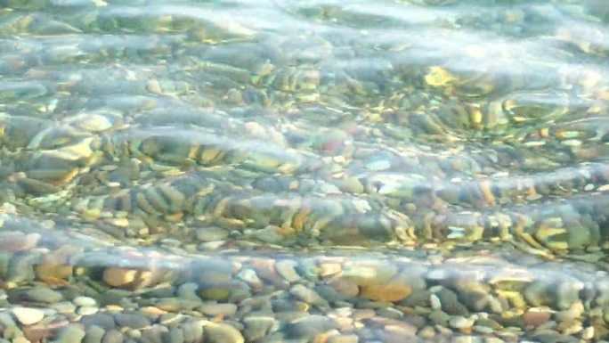 海边沙滩卵石。日落时分，海浪带着柔软的泡沫，冲刷着海滩上五颜六色的鹅卵石。没有人。假日休闲概念。抽象