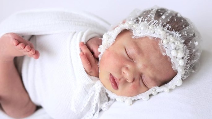 一个刚出生的女婴穿着尿布，戴着白色背景上漂亮的帽子，甜甜地睡着了，一个婴儿的诞生，一个幸福的家庭
