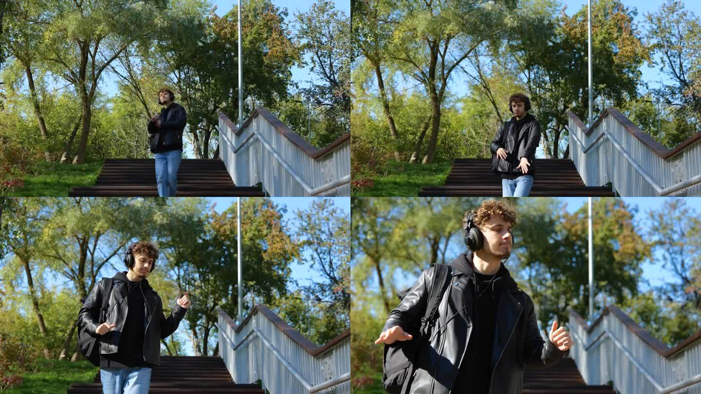 时髦的年轻人走下楼梯，在公园里戴着耳机听音乐，一边跳舞。的生活方式。秋季散步的概念。慢动作