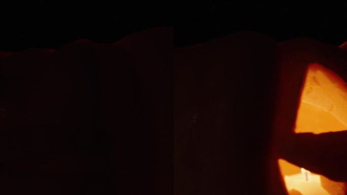 垂直视频。一个万圣节南瓜，旋转，从黑暗中出现。蜡烛在里面燃烧。