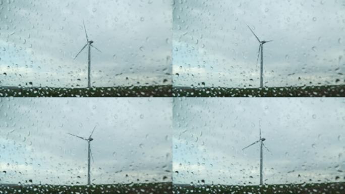 雨滴落在车窗上，背景是风车的景色。