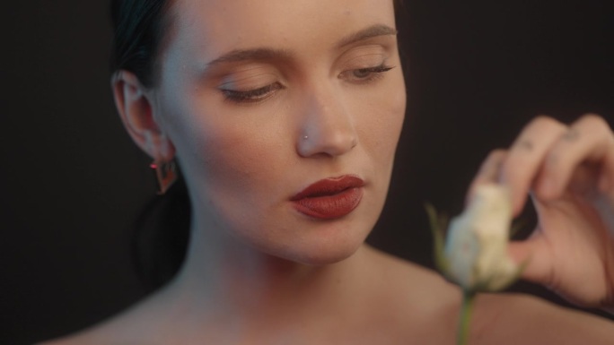 爱我的，不爱我的。性感的女人用红色的口红在摄影棚拍摄，她拿着一朵白玫瑰，正在采摘花瓣
