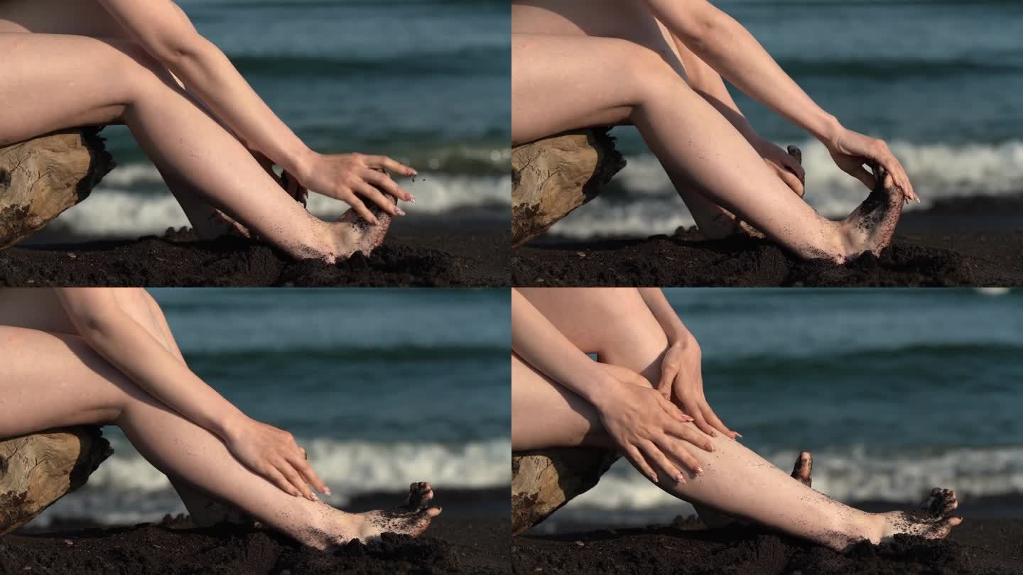 女人光着脚的特写，女人把脚从沙滩上的黑沙子上抖下来，坐在背景波上