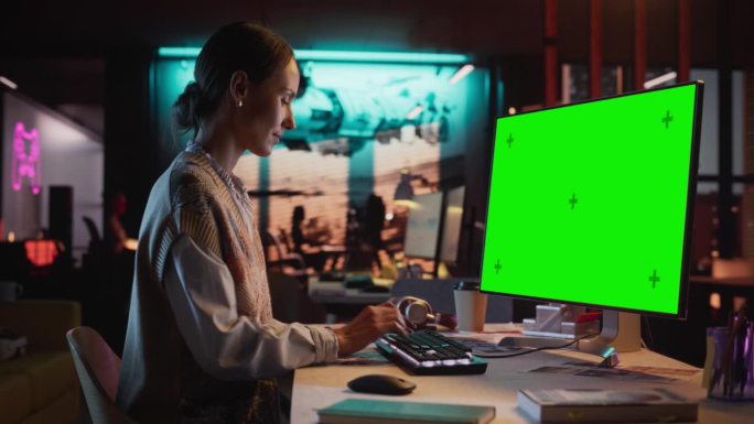 放大肖像的年轻女子坐在她的办公桌上使用台式电脑模拟绿屏。女性高加索专家工作与彩色键显示在创意机构的电