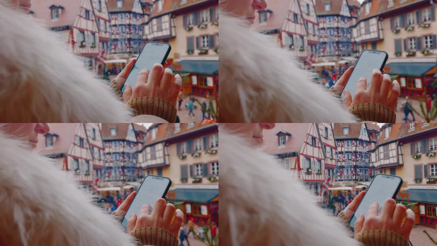 圣诞节期间，一名女子在科尔马镇广场上方一家酒店的阳台上使用她的智能手机