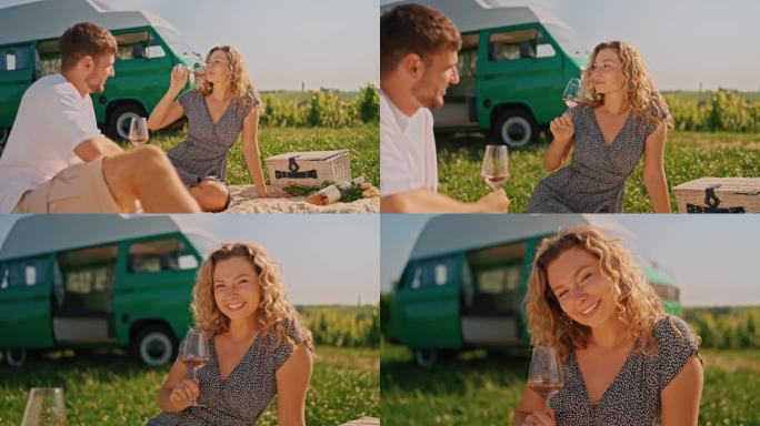 迷人女子微笑，与男友在葡萄园野餐毯上享用白葡萄酒