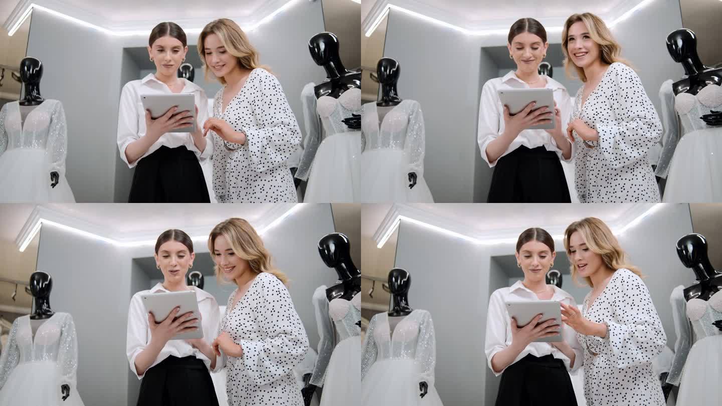 有吸引力的新娘店老板设计师女士用平板电脑帮助和支持顾客在商店选择婚纱
