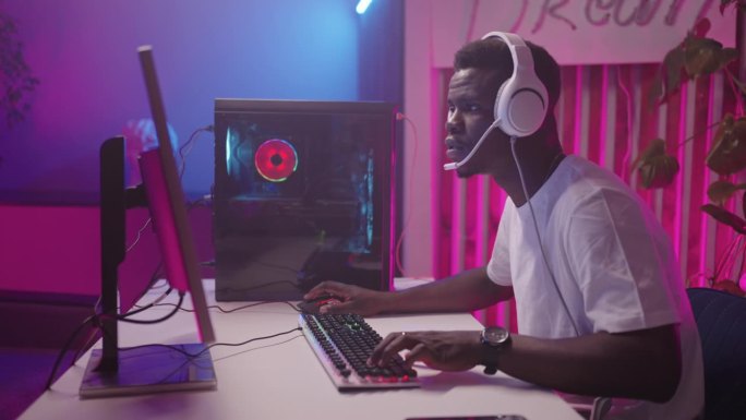 黑人在晚上玩网络游戏，沉迷于电子游戏的女士在电脑旁的肖像，网络中的娱乐和休闲，现代科技