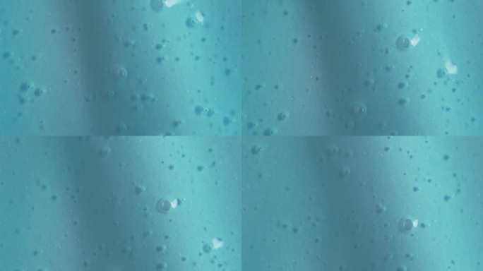 蓝色涂料化妆品的液滴在蓝色表面流动。蓝色沐浴露滴在墙上的微距镜头