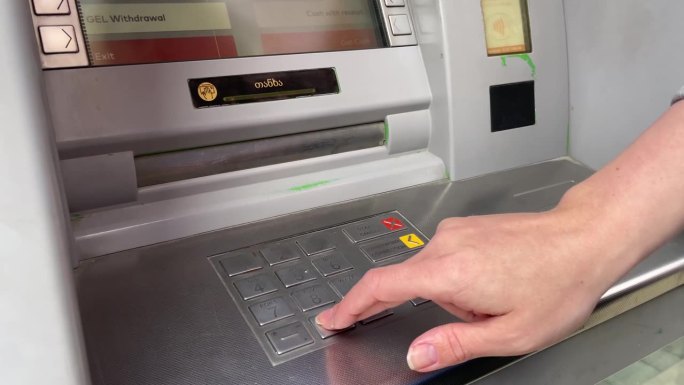 银行自动取款机，女士在键盘上输入密码取钱