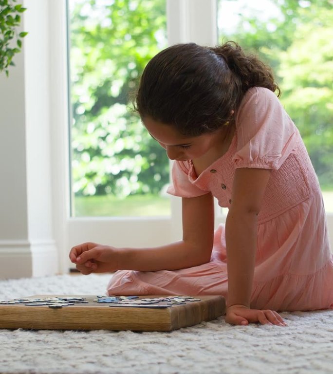 垂直视频的女孩在家里坐在地板上在休息室做拼图游戏