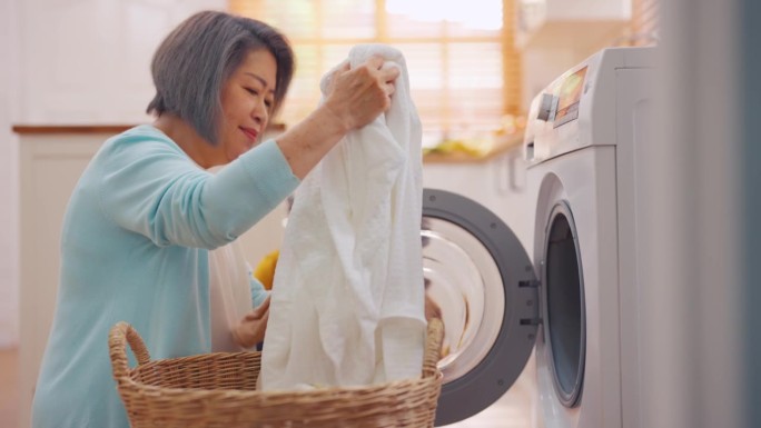 亚洲老年妇女和女儿把脏衣服放进洗衣机。有吸引力的成熟管家清洁，感觉很高兴在家里的洗衣机设备装载衣物。