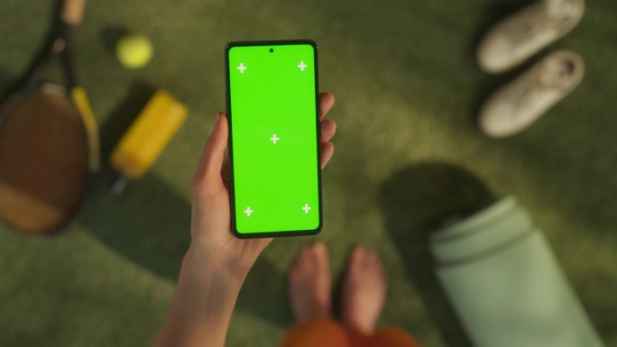 匿名女子在网球场上使用智能手机模拟绿屏Chromakey显示与运动跟踪占位符。视频模板内容促进健康的