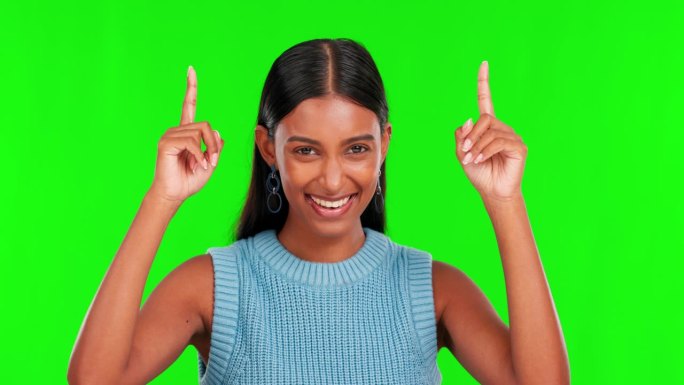 一个快乐的女人，指着上面的绿色屏幕，在一个工作室的背景下做广告或销售。在新闻、通知或市场营销中展示微