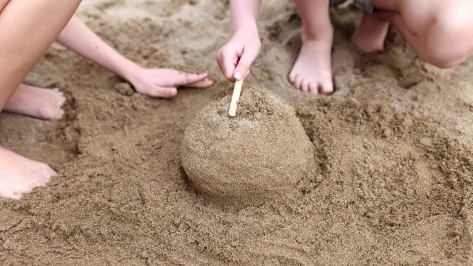 夏天，孩子们在海滩上用手玩耍，堆沙堡