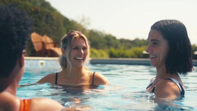 三个成熟的女性朋友穿着泳装在室外游泳池放松水疗日