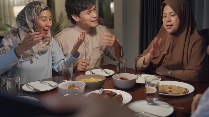 快乐的亚洲穆斯林家庭与表弟用手机视频在线庆祝异地斋月晚餐一起在家里。两代人一起庆祝开斋节。