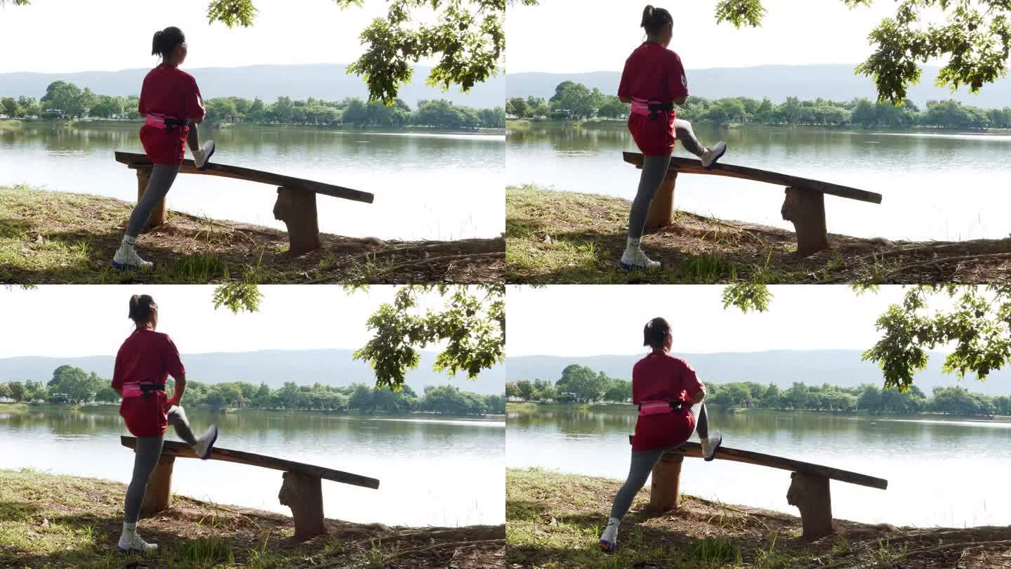 早晨，一位亚洲妇女在公园池塘边的长凳上暖脚。