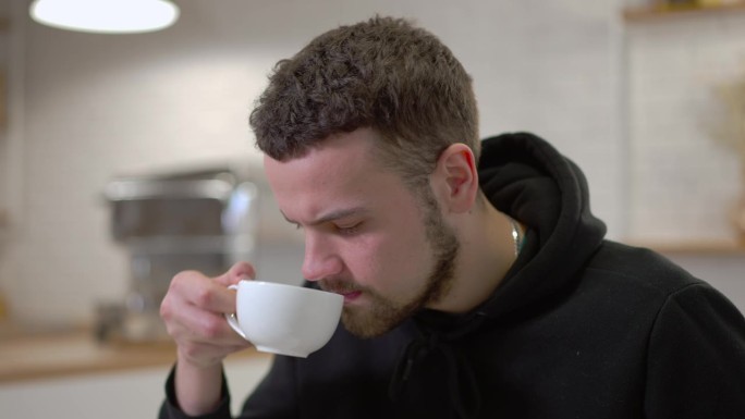 特写男子喝着难吃的咖啡味饮料，脸上带着不满的表情。咖啡馆室内不满意的白人男顾客画像。