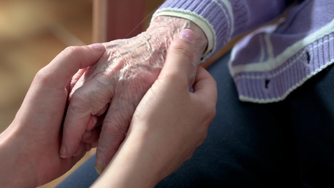 特写老年妇女的手与她的照顾者帮助的手握在一起，照顾者访问家中。家庭保健和养老院的概念。高品质4k画面