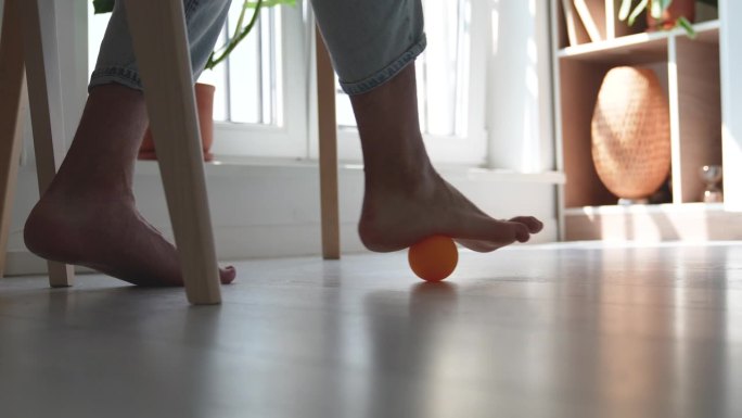 在长时间久坐不动的工作中，男子在桌子下使用硅胶球进行足部按摩。