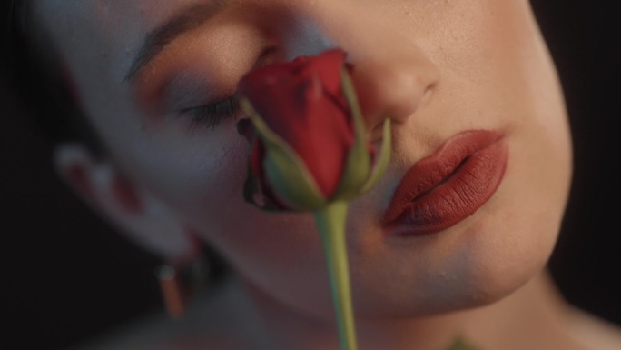 美丽性感的女人用红色的口红黑色的背景工作室拍摄的姿势亲吻一个红玫瑰和调情的镜头