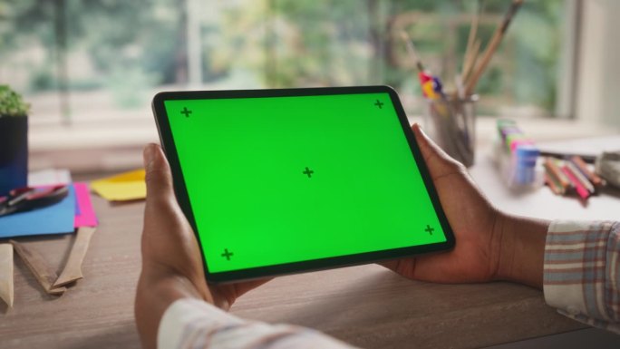 匿名自由设计师使用平板电脑与绿屏模拟显示的社交媒体张贴。一个人的手拿着一个设备与隔离区域的应用程序，