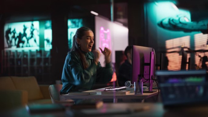 富有表现力的女性晚上坐在游戏开发公司的电脑前。兴奋的制作人很高兴并庆祝她的电子游戏在发行时获得了良好
